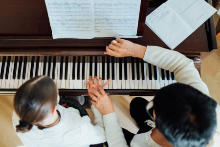 Muziekdocent begeleidt leerling op de piano en helpt bij de vingerzetting.