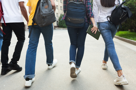 4 tieners lopen met schoolboeken en tassen op straat