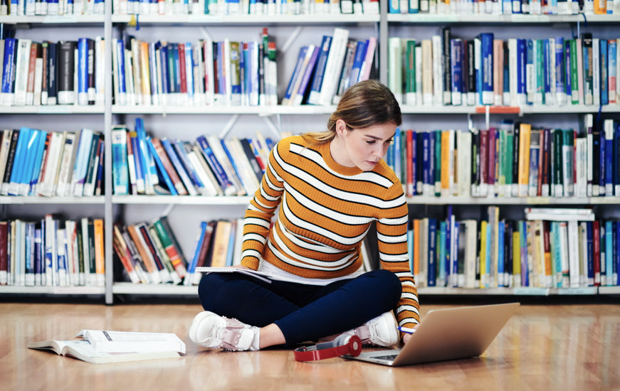 Jonge vrouw studeert al zittend op de grond in een bibliotheek