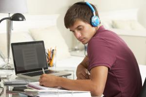 Jongen zit met koptelefoon op achter laptop en is aan het schrijven